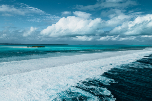 Aerial view of Aitutaki lagoon with turquoise waters coral reef breaking waves and a small island under a cloudy blue sky in Cook Islands. Aerial view of Aitutaki lagoon with turquoise waters coral reef breaking waves and a small island under a cloudy blue sky in Cook Islands.