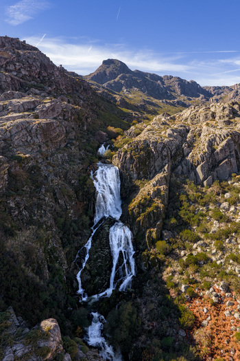Aerial view of the Vale da Candeeira waterfall cascading down rugged granite cliffs under a clear blue sky in Manteigas Distrito da Guarda Portugal. Aerial view of the Vale da Candeeira waterfall cascading down rugged granite cliffs under a clear blue sky in Manteigas Distrito da Guarda Portugal.