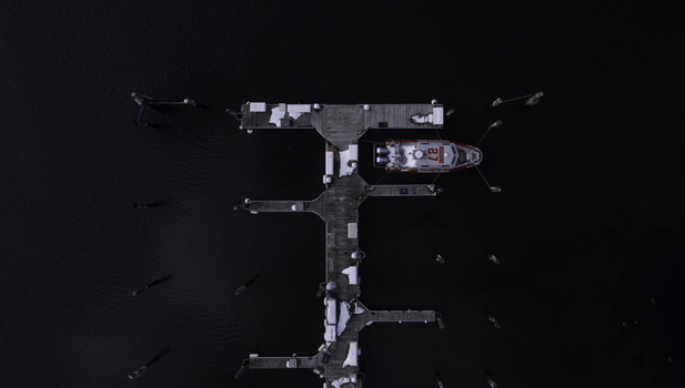 Aerial view of a red rescue boat docked at a wooden pier surrounded by dark water and patches of snow in Manasquan New Jersey United States. Aerial view of a red rescue boat docked at a wooden pier surrounded by dark water and patches of snow in Manasquan New Jersey United States.