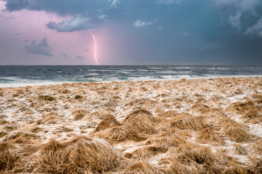 View of a lightning strike over the sea with a dramatic stormy sky above a beach covered in dry grass Leknes Lofoten Norway.