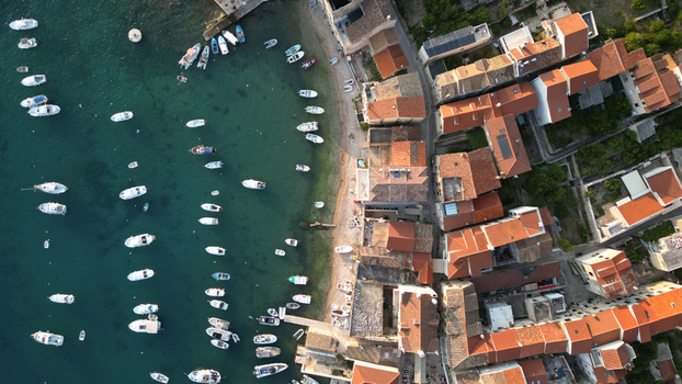 Aerial view of small boats moored in the harbor next to traditional red tiled houses and a narrow beach in Komiza Split Dalmatia County Croatia.