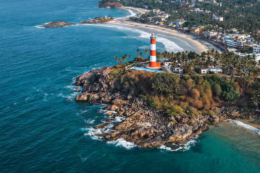 Aerial view of the red and white striped Vizhinjam Lighthouse on a rocky cliff overlooking the sandy beach and turquoise sea in Kovalam Kerala India. Aerial view of the red and white striped Vizhinjam Lighthouse on a rocky cliff overlooking the sandy beach and turquoise sea in Kovalam Kerala India.