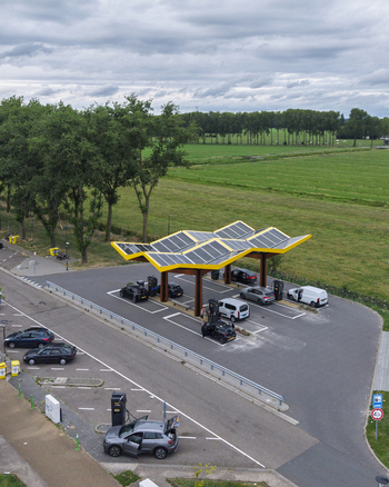 Aerial view of Fastned Charging Station with solar panel roof and electric vehicles charging in a rural landscape with green fields and trees in Beesd Gelderland Netherlands. Aerial view of Fastned Charging Station with solar panel roof and electric vehicles charging in a rural landscape with green fields and trees in Beesd Gelderland Netherlands.