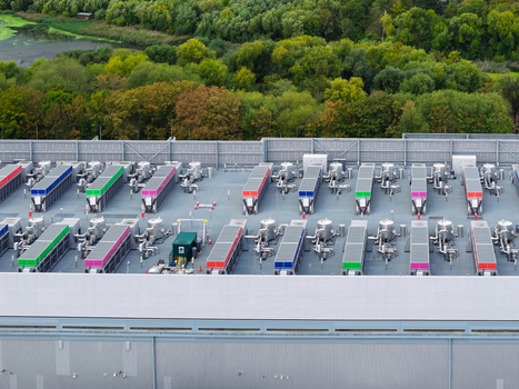 Aerial view of a data center roof featuring rows of colorful cooling units and ventilation systems set against a backdrop of lush green trees in the United Kingdom.