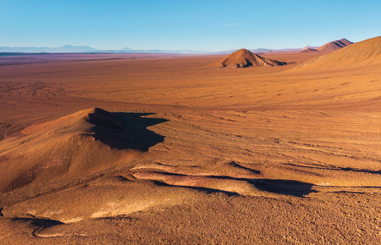 Aerial view of the vast arid landscape of the Atacama Desert with rolling hills and textured terrain under a clear blue sky in San Pedro de Atacama Antofagasta Chile. Aerial view of the vast arid landscape of the Atacama Desert with rolling hills and textured terrain under a clear blue sky in San Pedro de Atacama Antofagasta Chile.