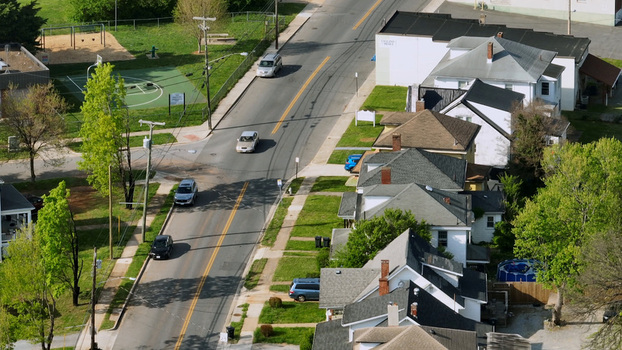 Aerial view of a quiet residential street lined with houses lush green trees and cars driving along the road in Lynchburg Virginia United States.