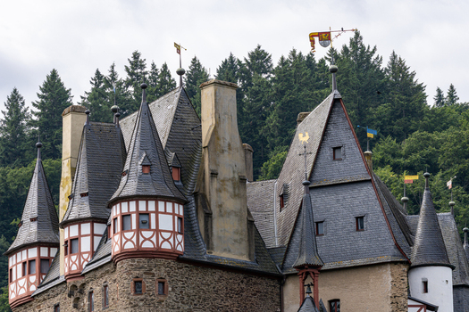 View of Eltz Castle featuring its medieval towers with half timbered architecture and slate roofs against a backdrop of lush green forest in Wierschem Rhineland Palatinate Germany.