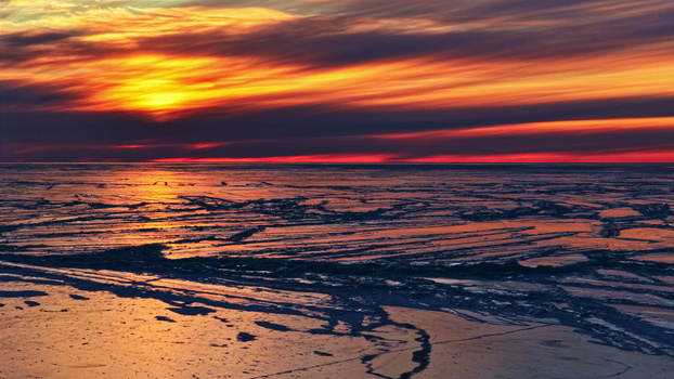Aerial view of the frozen sea surface with cracked ice patterns reflecting the vibrant orange and red colors of a sunset in Latvia. Aerial view of the frozen sea surface with cracked ice patterns reflecting the vibrant orange and red colors of a sunset in Latvia.