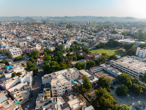 Aerial view of the dense urban landscape of Udaipur featuring residential buildings green spaces and distant hills under a clear sky in Udaipur Rajasthan India.