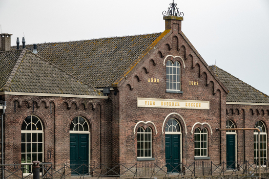 View of the historic brick facade of the Dutch Steam Engine Museum with arched windows and tiled roofs under an overcast sky in Medemblik Noord Holland Netherlands. View of the historic brick facade of the Dutch Steam Engine Museum with arched windows and tiled roofs under an overcast sky in Medemblik Noord Holland Netherlands.