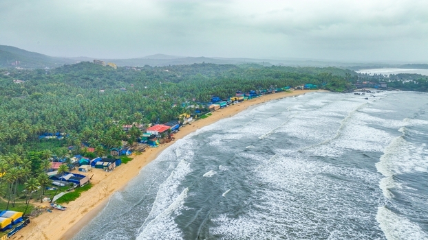 Aerial view of Palolem Beach with its sandy shore lush palm trees colorful beach huts and waves crashing on the coastline in Canacona Goa India.