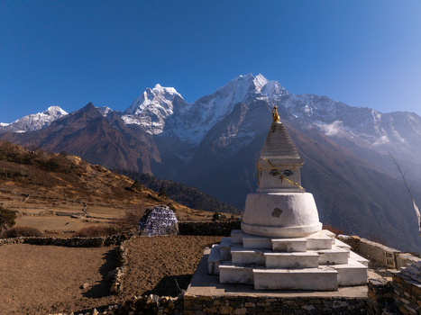 Aerial view of a white Buddhist stupa with prayer flags set against the backdrop of snow capped Himalayan mountains in Nepal.