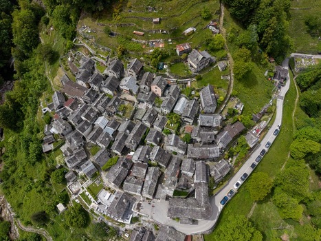 Aerial view of Corippo Albergo Diffuso featuring traditional stone houses nestled on a steep green hillside with a winding road Corippo Ticino Switzerland. Aerial view of Corippo Albergo Diffuso featuring traditional stone houses nestled on a steep green hillside with a winding road Corippo Ticino Switzerland.