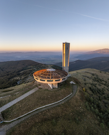 Aerial view of the abandoned brutalist Buzludzha Monument atop a mountain peak at sunset with rolling hills and clear sky in Stara Zagora Bulgaria. Aerial view of the abandoned brutalist Buzludzha Monument atop a mountain peak at sunset with rolling hills and clear sky in Stara Zagora Bulgaria.