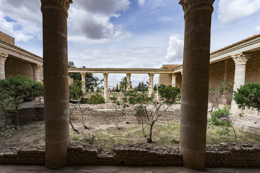View of the ancient stone columns and courtyard ruins of the Amphitheatre of El Jem under a cloudy sky in El Jem Gouvernorat de Mahdia Tunisia.