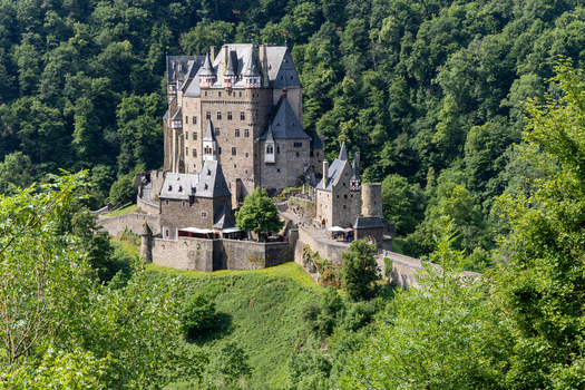 View of Eltz Castle surrounded by dense green forest and stone fortifications under bright daylight Wierschem Rhineland Palatinate Germany.