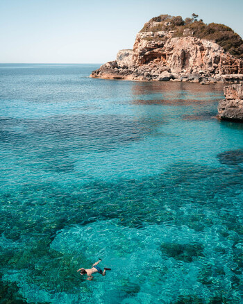 Balearic Islands Spain 15 September 2023 View of a person snorkeling in the clear turquoise waters of the Mediterranean Sea near the rocky coastline of Mallorca. Balearic Islands Spain 15 September 2023 View of a person snorkeling in the clear turquoise waters of the Mediterranean Sea near the rocky coastline of Mallorca.