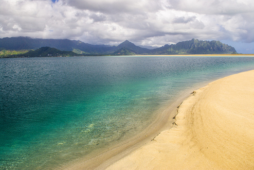 View of Kaneohe Bay with turquoise water a sandy beach and mountains under a cloudy sky in Honolulu County Hawaii United States. View of Kaneohe Bay with turquoise water a sandy beach and mountains under a cloudy sky in Honolulu County Hawaii United States.