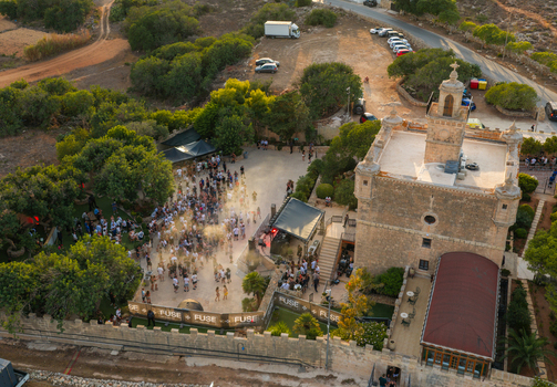 Northern Region Malta 17 September 2026 Aerial view of an outdoor music event at a historic stone tower with a crowd gathered in the courtyard surrounded by trees and rural terrain. Northern Region Malta 17 September 2026 Aerial view of an outdoor music event at a historic stone tower with a crowd gathered in the courtyard surrounded by trees and rural terrain.