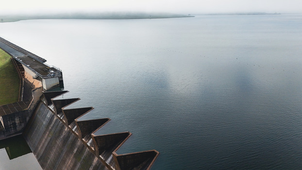 Aerial view of Midmar Dam featuring the concrete wall and calm water under a misty sky in Howick KwaZulu Natal South Africa. Aerial view of Midmar Dam featuring the concrete wall and calm water under a misty sky in Howick KwaZulu Natal South Africa.