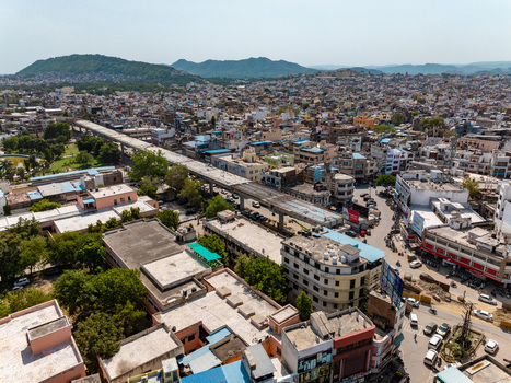 Aerial view of the dense urban landscape featuring an elevated highway cutting through the city with surrounding residential buildings and distant hills in Udaipur Rajasthan India.