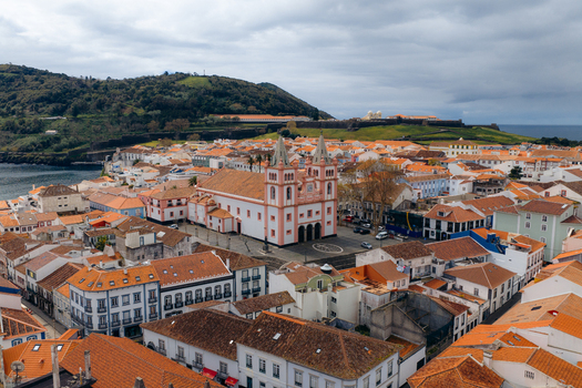 Aerial view of the historic Se Catedral de Angra do Heroismo surrounded by traditional orange tiled rooftops and green hills under a cloudy sky in Angra do Heroismo Azores Portugal.