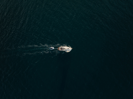 Aerial view of a white sailboat towing a small dinghy across the deep blue sea in Syracuse Sicily Italy. Aerial view of a white sailboat towing a small dinghy across the deep blue sea in Syracuse Sicily Italy.