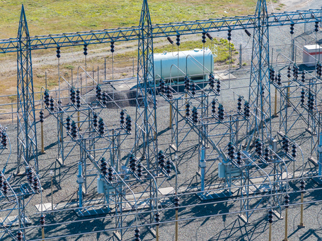 Aerial view of an electrical substation featuring metal lattice towers high voltage insulators and a large storage tank on a gravel ground in Bandon Oregon United States. Aerial view of an electrical substation featuring metal lattice towers high voltage insulators and a large storage tank on a gravel ground in Bandon Oregon United States.