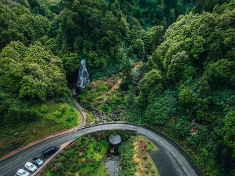 Aerial view of a cascading waterfall plunging into a verdant valley embraced by dense forest and a winding road near Estrada Regional Achada Achada Açores Portugal. Aerial view of a cascading waterfall plunging into a verdant valley embraced by dense forest and a winding road near Estrada Regional Achada Achada Açores Portugal.