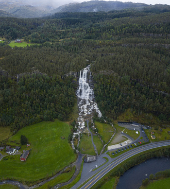 Aerial view of the Tvindefossen waterfall cascading down a steep rocky cliff surrounded by dense green forest and lush meadows.