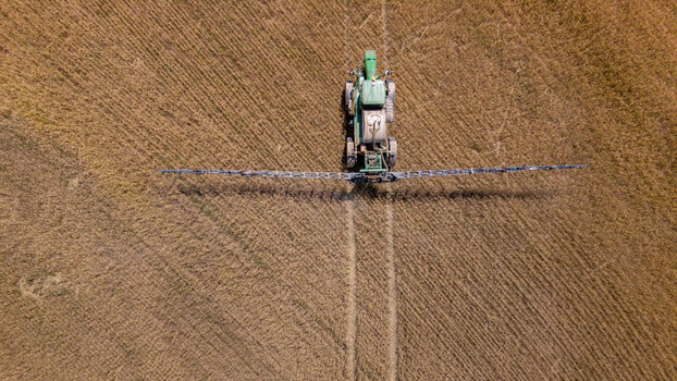 Aerial view of a green tractor spraying a large agricultural field with visible tire tracks in the soil in Philadelphia Western Cape South Africa. Aerial view of a green tractor spraying a large agricultural field with visible tire tracks in the soil in Philadelphia Western Cape South Africa.