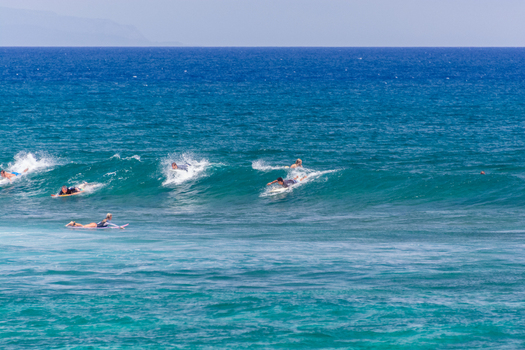 View of surfers paddling and riding waves in the clear blue ocean off the coast of Maui Maui County Hawaii United States.