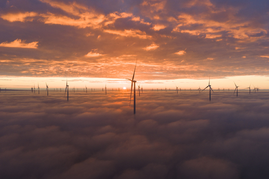 Aerial view of wind turbines rising above a thick blanket of clouds during a vibrant orange sunset over the Afsluitdijk dam Breezanddijk Friesland Netherlands. Aerial view of wind turbines rising above a thick blanket of clouds during a vibrant orange sunset over the Afsluitdijk dam Breezanddijk Friesland Netherlands.