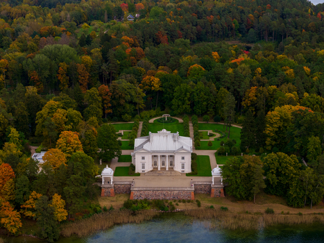 Aerial view of Uzutrakis Manor with its white neoclassical facade and formal gardens surrounded by colorful autumn forest in Trakai Vilniaus apskritis Lithuania.
