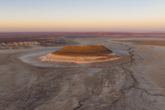 Aerial view of a majestic layered butte rising from the arid desert floor under a soft golden sunset sky in the Mangystau Region Kazakhstan. Aerial view of a majestic layered butte rising from the arid desert floor under a soft golden sunset sky in the Mangystau Region Kazakhstan.