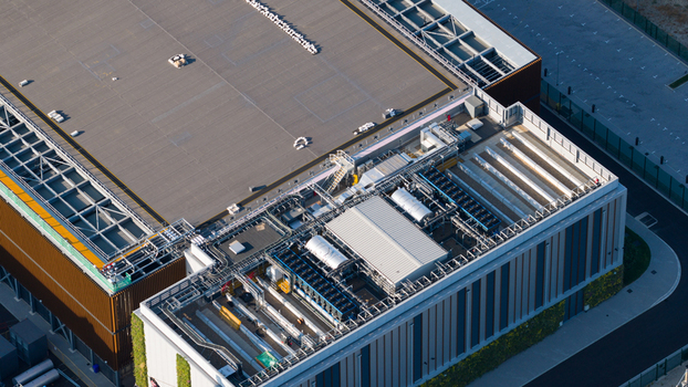 Aerial view of a modern industrial facility featuring complex rooftop HVAC infrastructure and solar panels in Longcross England United Kingdom.