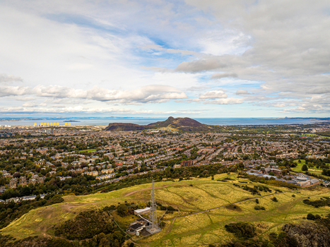 Aerial view of Arthur s Seat and the cityscape with lush green hills urban residential areas and the Firth of Forth in the background Edinburgh Scotland United Kingdom.