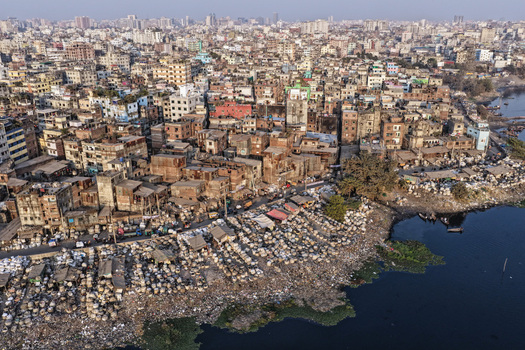 Aerial view of the dense urban landscape along the Buriganga River featuring crowded buildings and a riverbank cluttered with waste and small boats in Dhaka Dhaka Division Bangladesh. Aerial view of the dense urban landscape along the Buriganga River featuring crowded buildings and a riverbank cluttered with waste and small boats in Dhaka Dhaka Division Bangladesh.