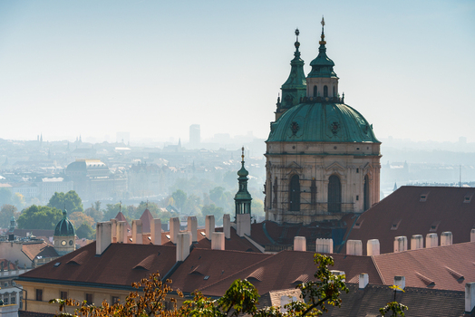 View of the green copper dome and towers of St. Nicholas Church rising above the red tiled rooftops of the historic city center in Prague Prague Czechia.