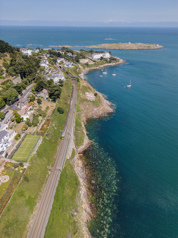 Aerial view of the coastal railway line passing through Dalkey with Dalkey Island in the background featuring rocky cliffs residential houses and the Irish Sea in Dublin County Dublin Ireland. Aerial view of the coastal railway line passing through Dalkey with Dalkey Island in the background featuring rocky cliffs residential houses and the Irish Sea in Dublin County Dublin Ireland.