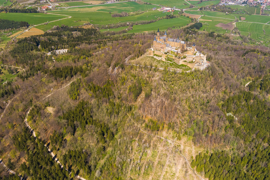 Burg Hohenzollern Germany 27 September 2026 Aerial view of Hohenzollern Castle perched atop a forested mountain peak surrounded by green fields and rolling hills under a clear sky.