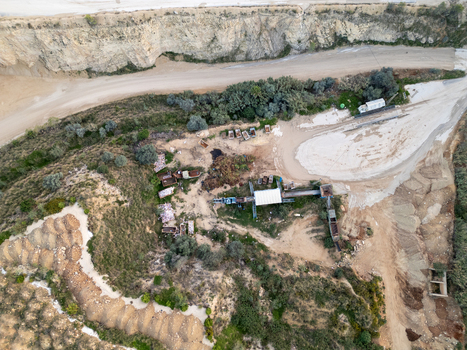 Aerial view of industrial quarry site with machinery and piles of excavated earth surrounded by rocky terrain and vegetation in Teulada Valencian Community Spain.