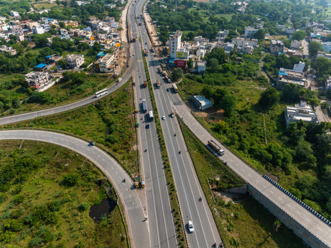 Aerial view of a highway interchange with vehicles traveling on asphalt roads surrounded by green vegetation and urban buildings in Udaipur Rajasthan India. Aerial view of a highway interchange with vehicles traveling on asphalt roads surrounded by green vegetation and urban buildings in Udaipur Rajasthan India.
