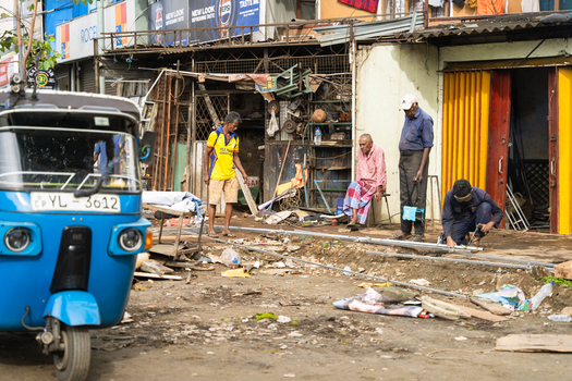 Sri Lanka 20 February 2026 View of men working on metal pipes outside a workshop with a blue tuk tuk parked in the foreground on a street in Sri Lanka.