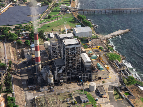 Aerial view of the industrial power plant complex featuring a tall smokestack solar panels and coastal infrastructure in Bajos de Haina San Cristobal Province Dominican Republic.
