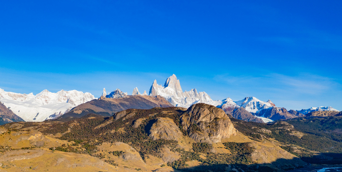 Aerial view of the snow capped peaks of Mount Fitz Roy rising above the golden brown hills and rocky terrain of the Patagonia wilderness in El Chalten Santa Cruz Argentina. Aerial view of the snow capped peaks of Mount Fitz Roy rising above the golden brown hills and rocky terrain of the Patagonia wilderness in El Chalten Santa Cruz Argentina.