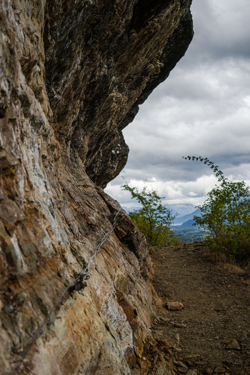 View of the rugged rock face of Indian Head with a safety wire along the hiking trail under a cloudy sky in Bariloche Department Rio Negro Province Argentina. View of the rugged rock face of Indian Head with a safety wire along the hiking trail under a cloudy sky in Bariloche Department Rio Negro Province Argentina.