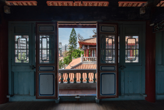 View of the traditional architecture of Chihkan Tower framed by ornate wooden doors looking out over tiled rooftops and lush trees in Chihkan Village Tainan City Taiwan. View of the traditional architecture of Chihkan Tower framed by ornate wooden doors looking out over tiled rooftops and lush trees in Chihkan Village Tainan City Taiwan.