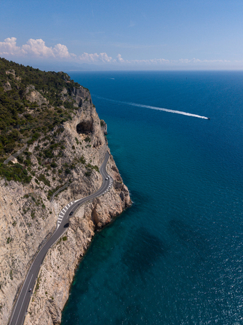 Aerial view of the winding coastal road along the steep cliffs of Sentiero del Pellegrino overlooking the turquoise Mediterranean Sea Noli Liguria Italy.