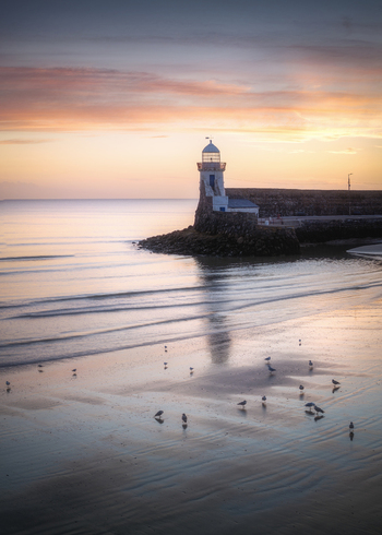 Aerial view of Balbriggan Harbour with its iconic lighthouse standing on the pier at sunset with seagulls on the wet sand of the beach in Balbriggan County Dublin Ireland. Aerial view of Balbriggan Harbour with its iconic lighthouse standing on the pier at sunset with seagulls on the wet sand of the beach in Balbriggan County Dublin Ireland.